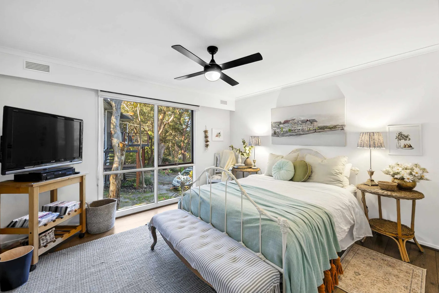 A bright bedroom with a large bed, bedside tables, and wide windows.