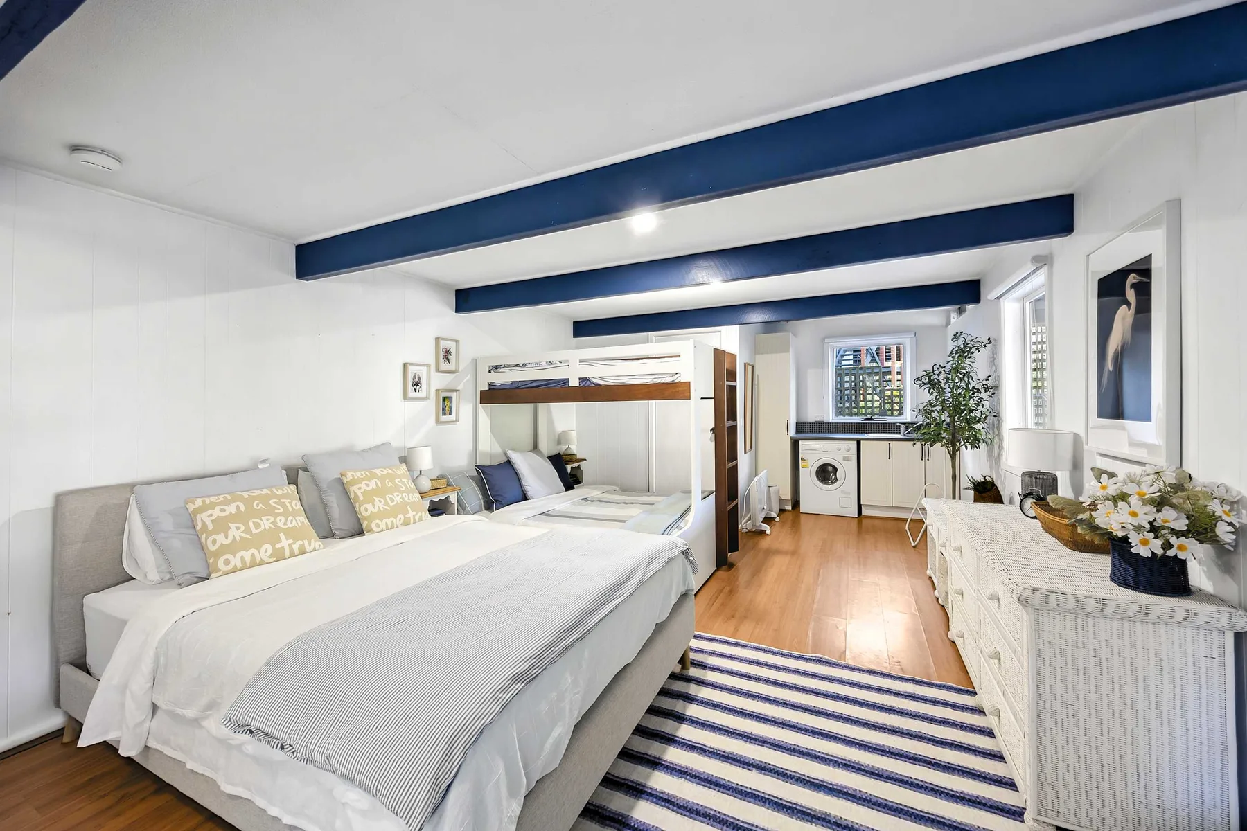 A bright bedroom with beds, a striped rug, and a dresser.