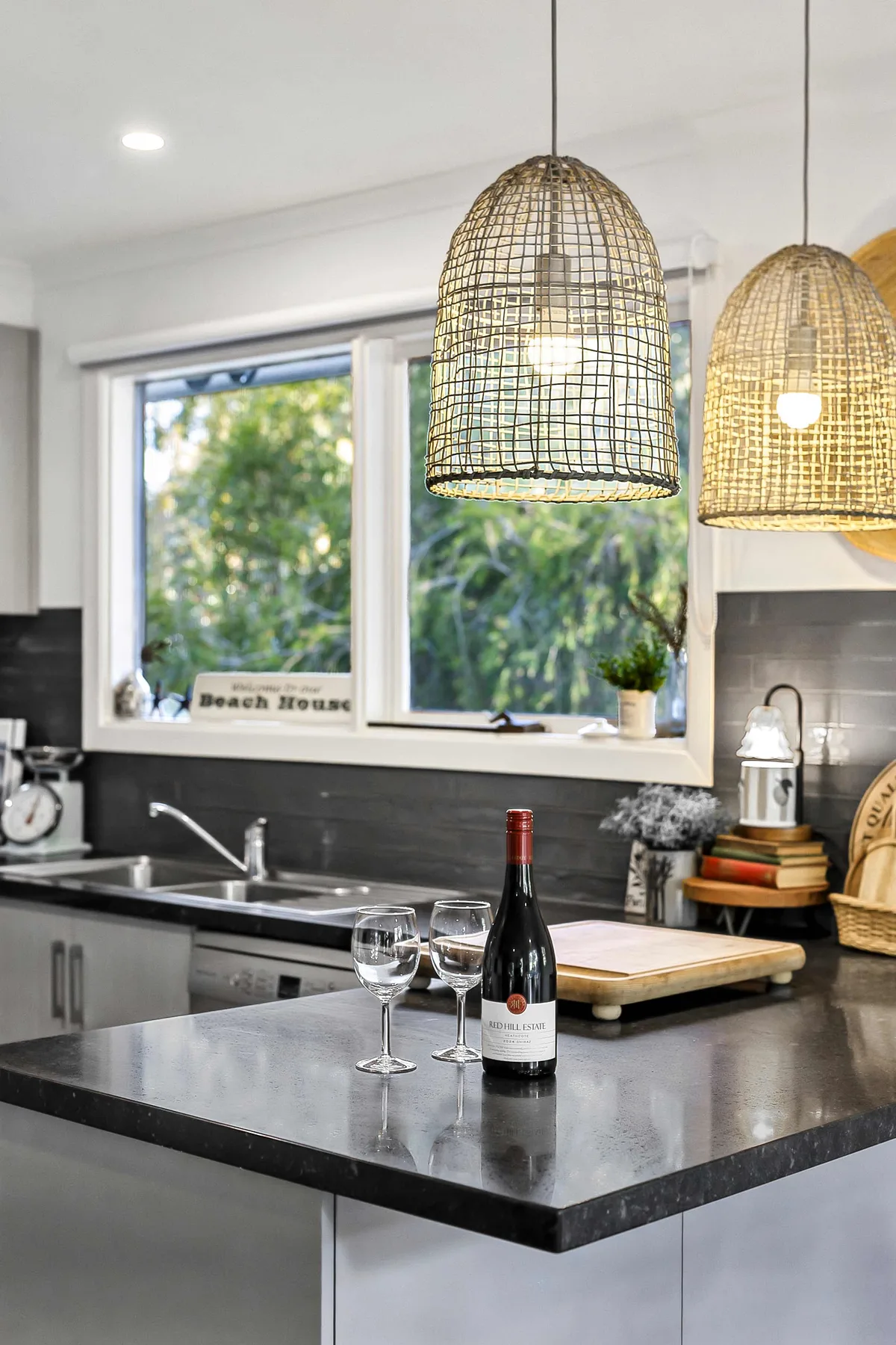 A bright kitchen with a dark countertop and woven pendant lights.
