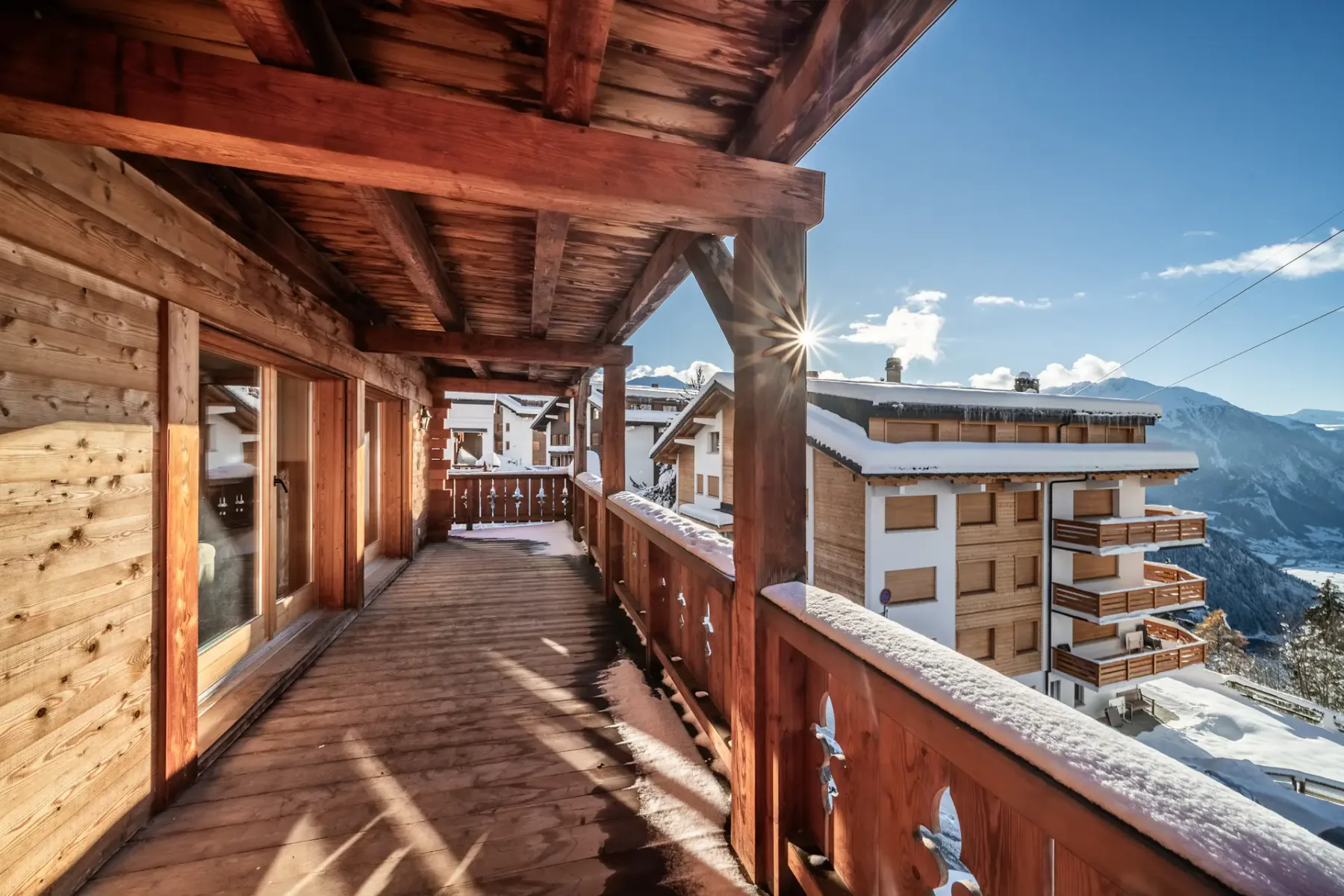 A wooden balcony overlooking snowy mountains and a ski lift.