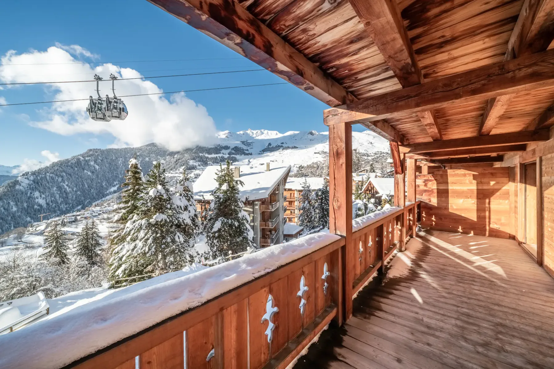 A wooden balcony overlooking snowy mountains and a ski lift.