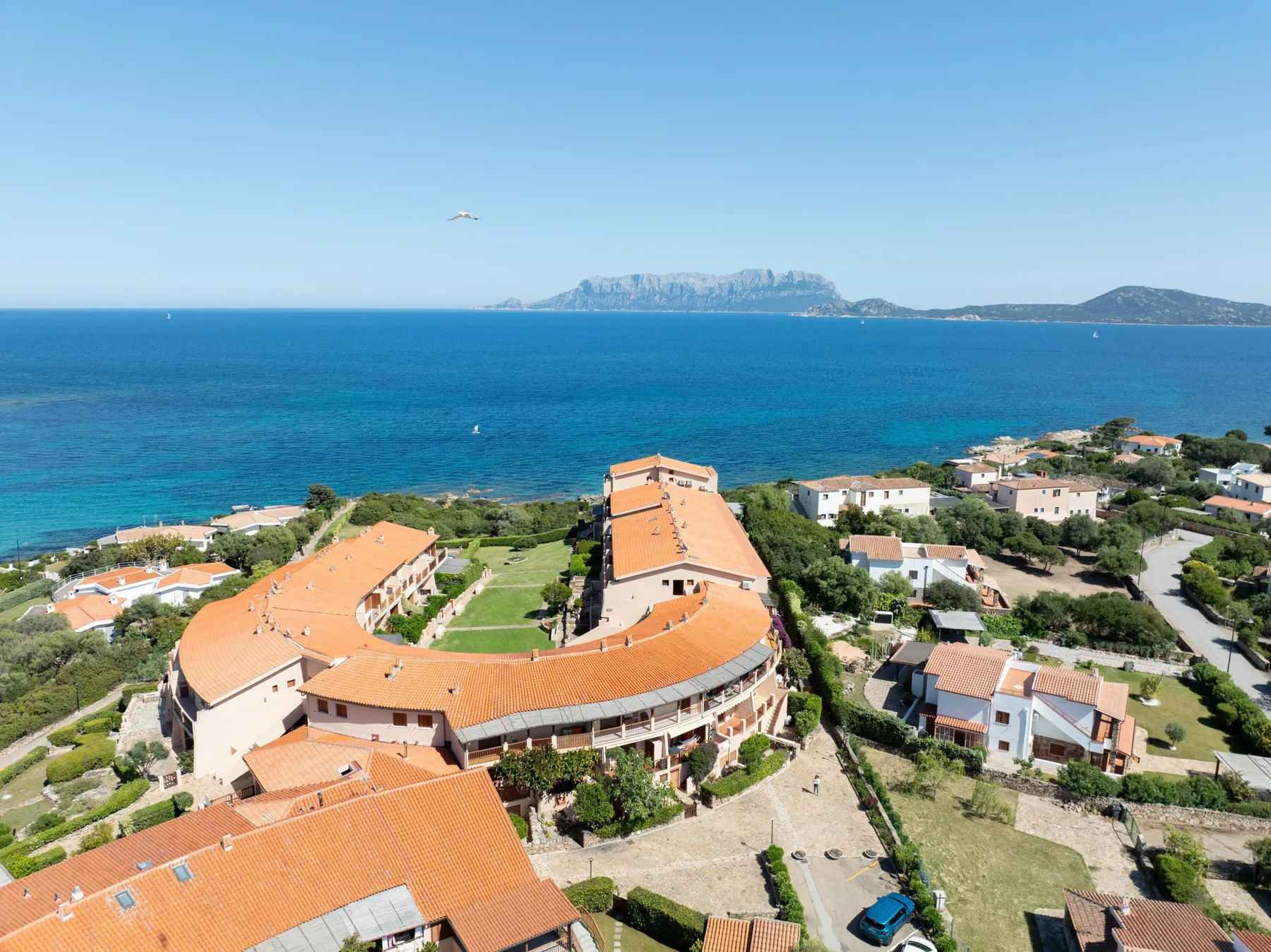 Vista aérea de un complejo costero con edificios de tejados de terracota junto al mar.