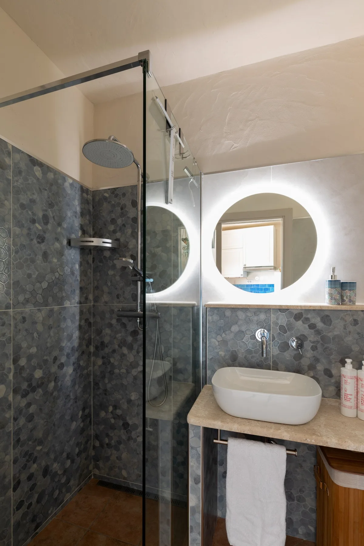 Un baño con ducha de vidrio, espejo redondo y lavabo sobre encimera.