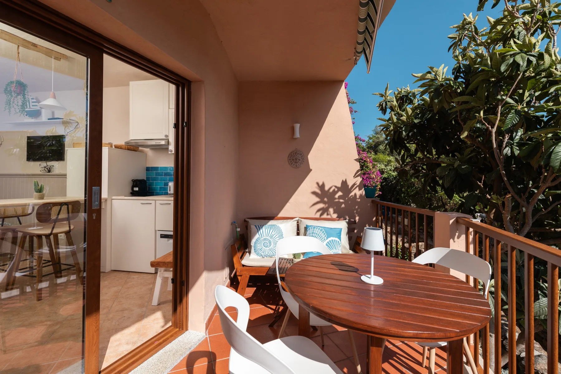 Un patio soleado con una mesa de madera y asientos blancos.