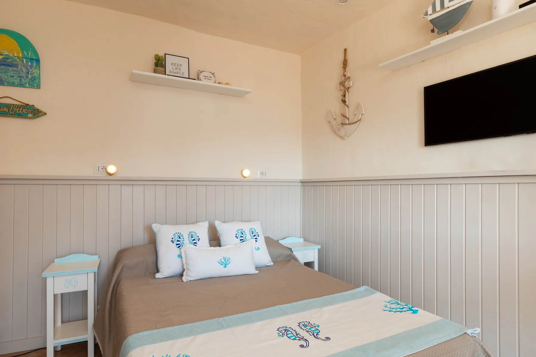 Un dormitorio con una cama, paredes claras con paneles y un televisor en la pared.