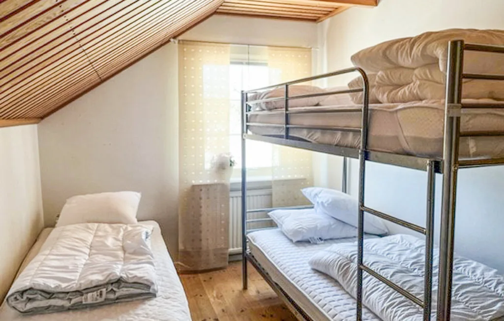 Un dormitorio con literas y una cama individual bajo un techo inclinado de madera.