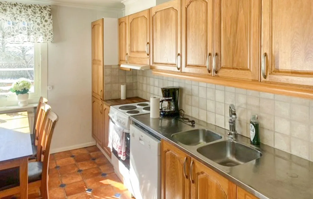 Una cocina luminosa con armarios de madera, salpicadero de azulejos y una mesa junto a la ventana.