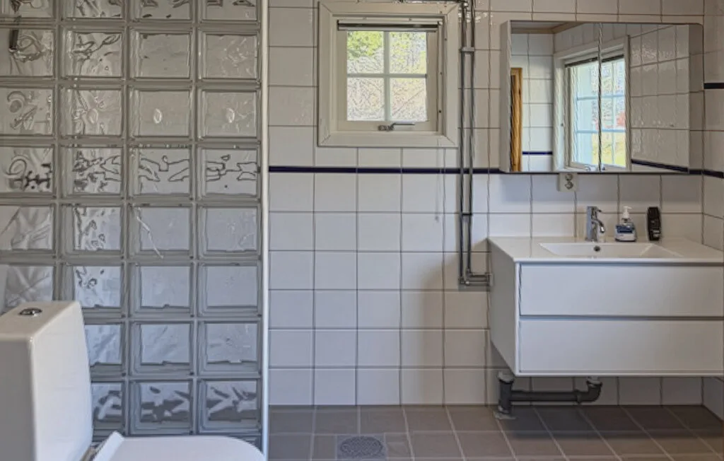 Un baño alicatado con una pared de bloques de vidrio y un lavabo suspendido.