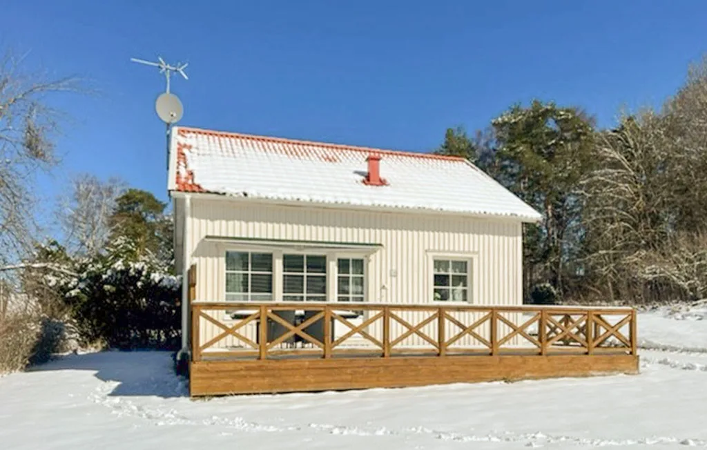 Una casa pequeña con una larga terraza de madera se alza entre la nieve bajo un cielo azul despejado.