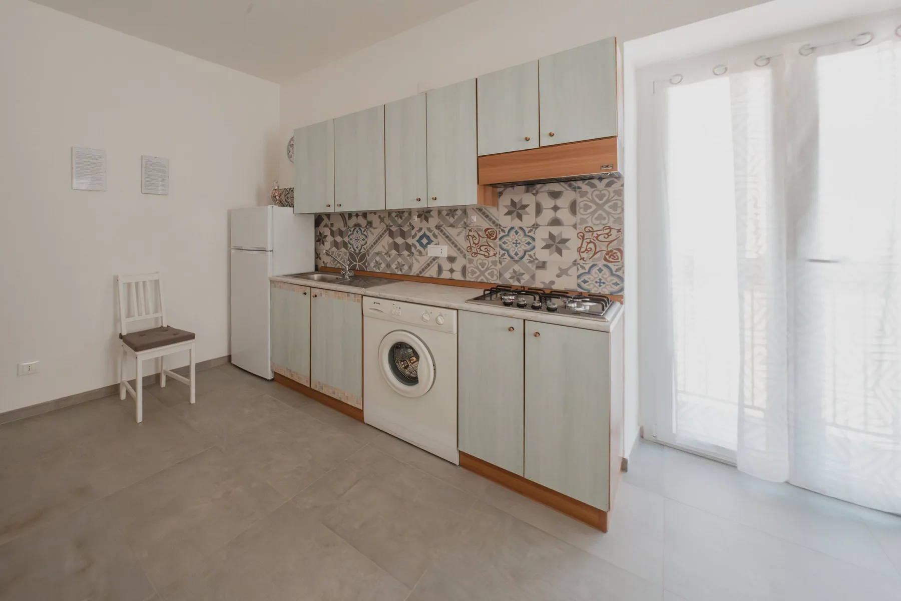A compact kitchen with pale cabinets, a patterned backsplash, and a washing machine.
