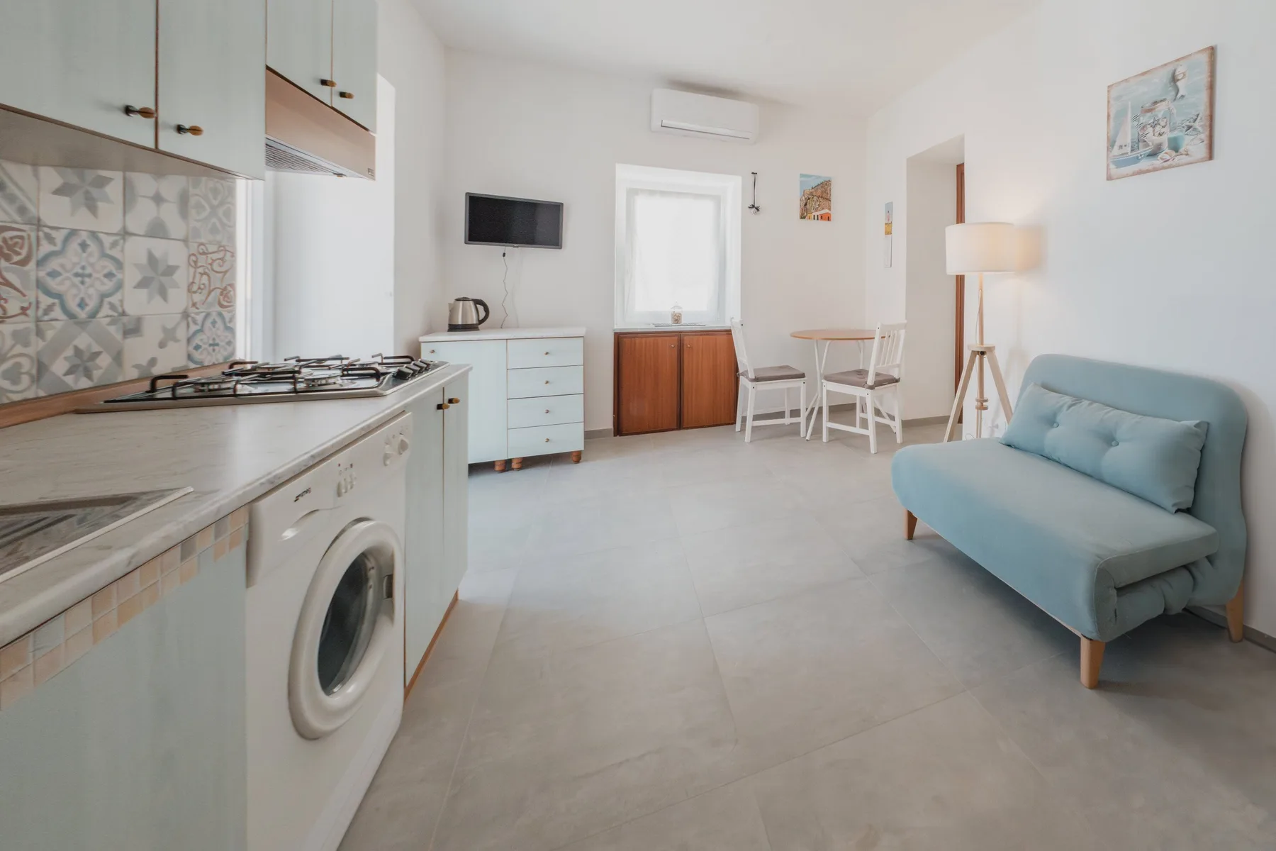 A bright kitchen and living area with a small table and blue seating.