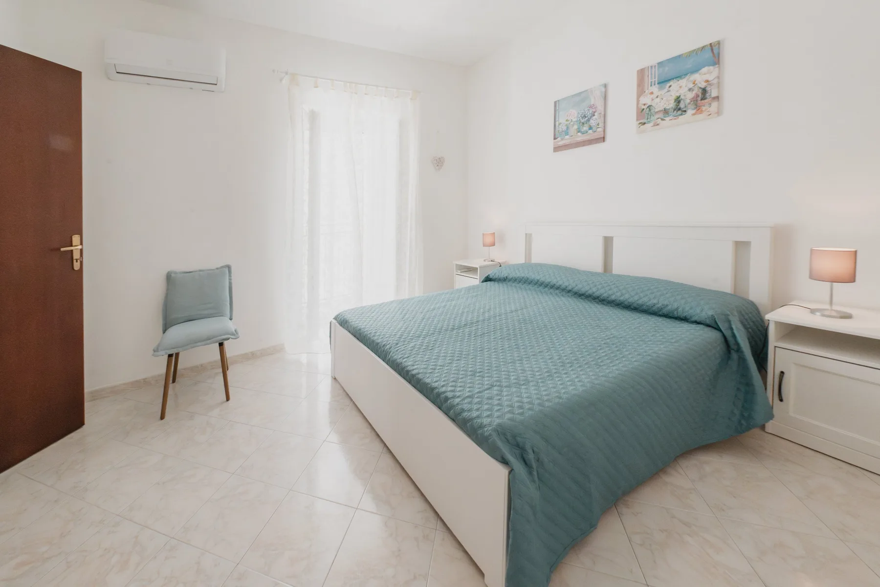 A bright bedroom with a neatly made bed and a chair beside the window.