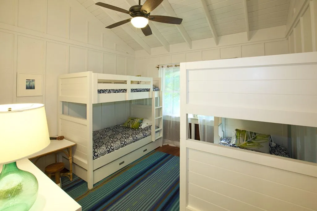 A bright bunk bedroom with built-in beds, a striped rug, and a ceiling fan.
