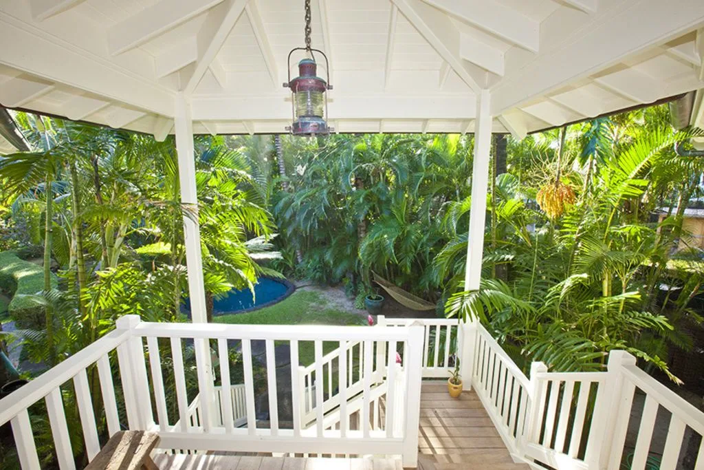 A covered wooden porch overlooks dense tropical greenery and a small pool.
