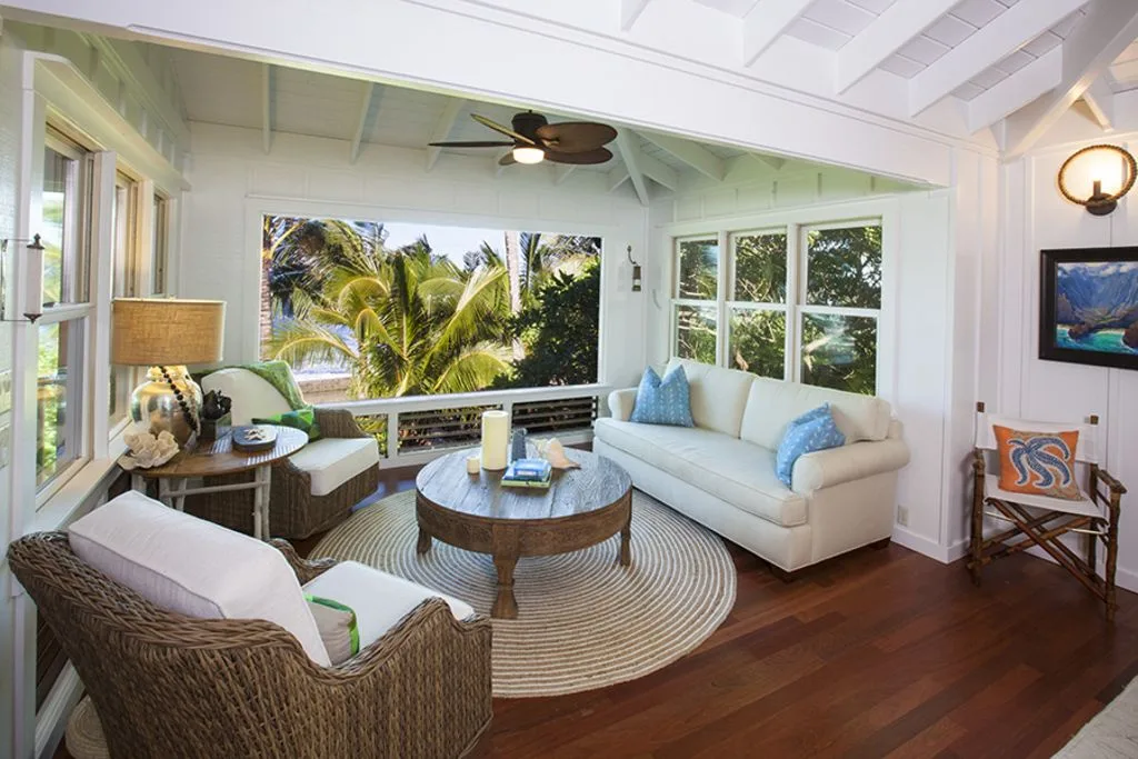 A bright living room with seating around a round coffee table and windows overlooking palm trees.