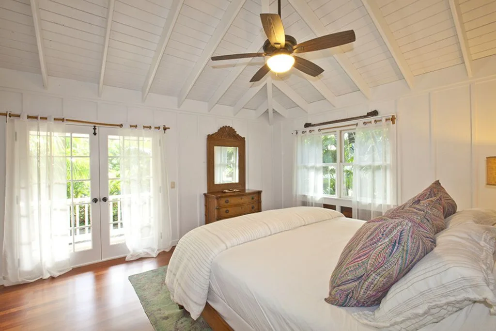 A bright bedroom with a bed, windows, and a ceiling fan.