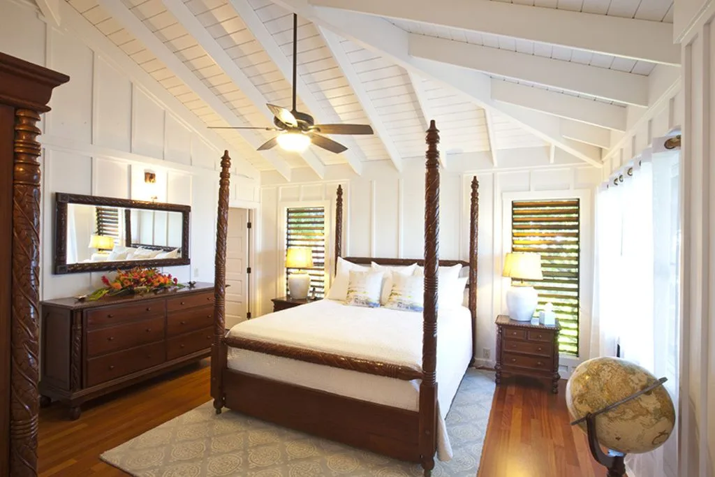 A bedroom with a four-poster bed, wooden furniture, and a ceiling fan.