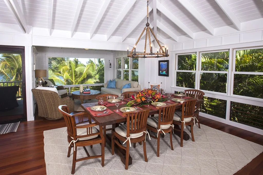 A bright dining area with a wooden table and chairs beside large windows.