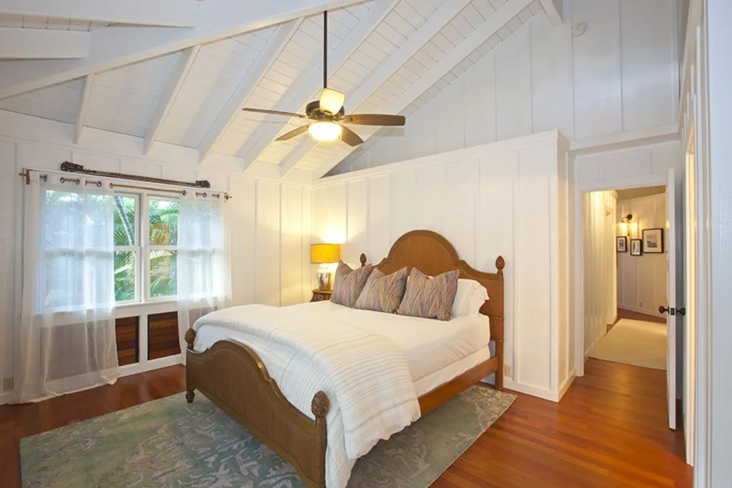 A bright bedroom with a wooden bed, white bedding, and a sloped ceiling.