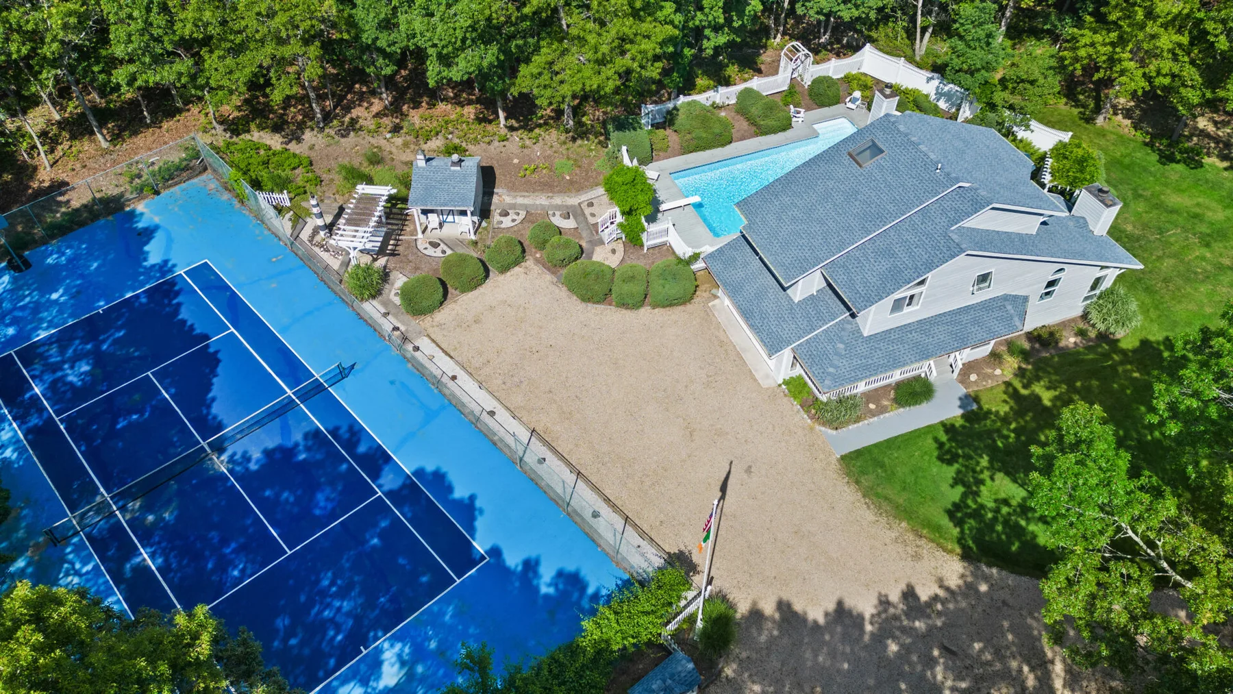 Una vista aérea muestra una casa junto a una cancha de tenis y una piscina.