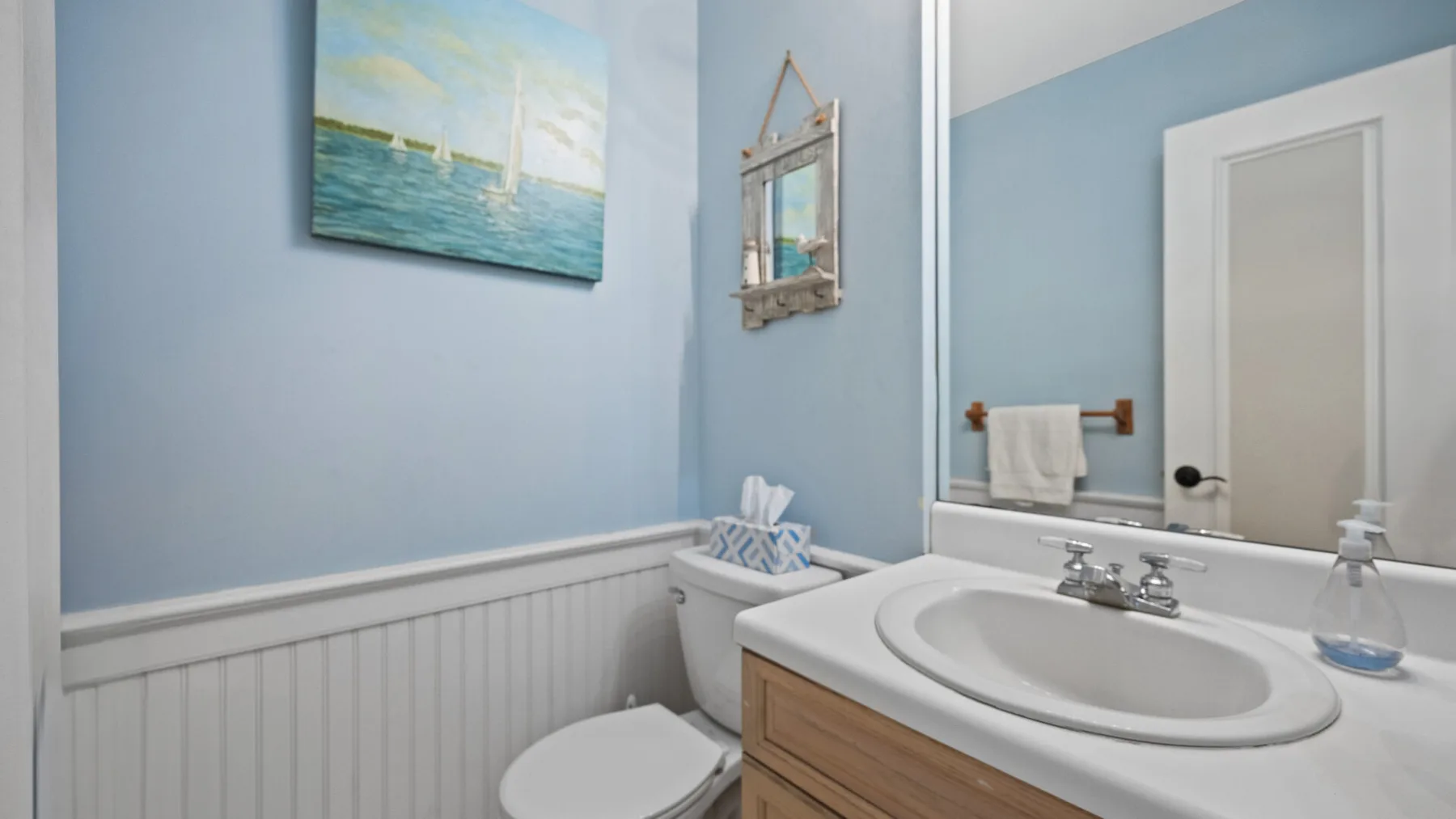 Un baño con lavabo, inodoro y arte costero en la pared.