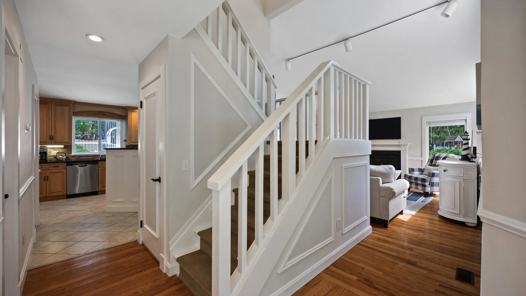 Un interior luminoso muestra una escalera blanca junto a una sala de estar y una cocina.