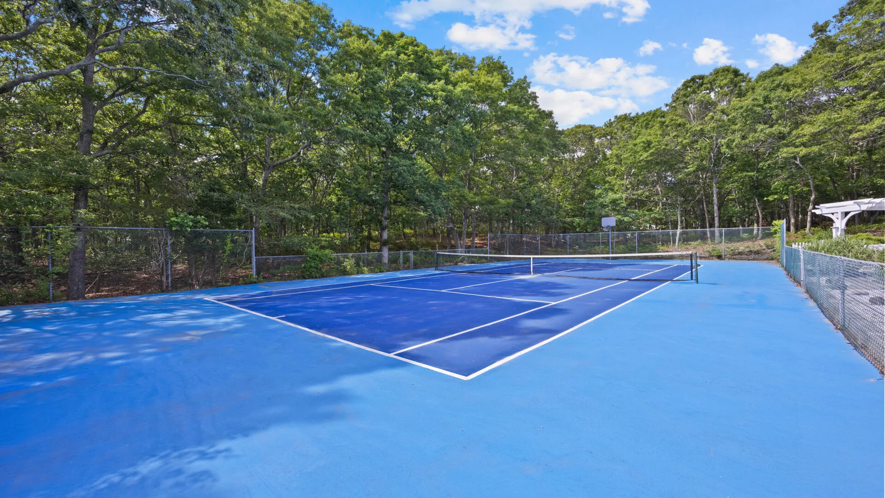 Una cancha de tenis al aire libre rodeada de árboles bajo un cielo parcialmente nublado.