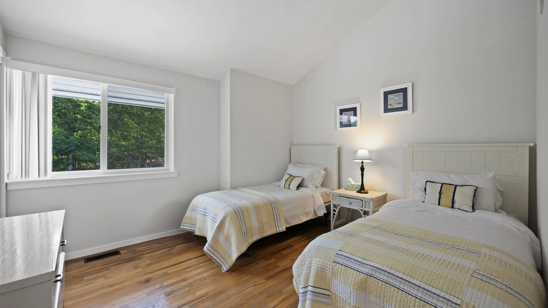 Un dormitorio luminoso con dos camas y una ventana grande con vistas a la vegetación.