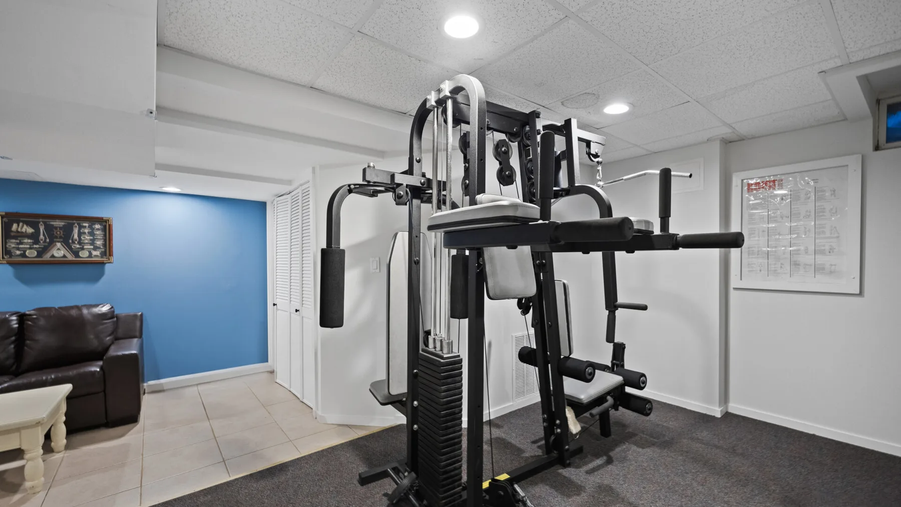 Un gimnasio en el sótano con una máquina de ejercicios y una zona de descanso.