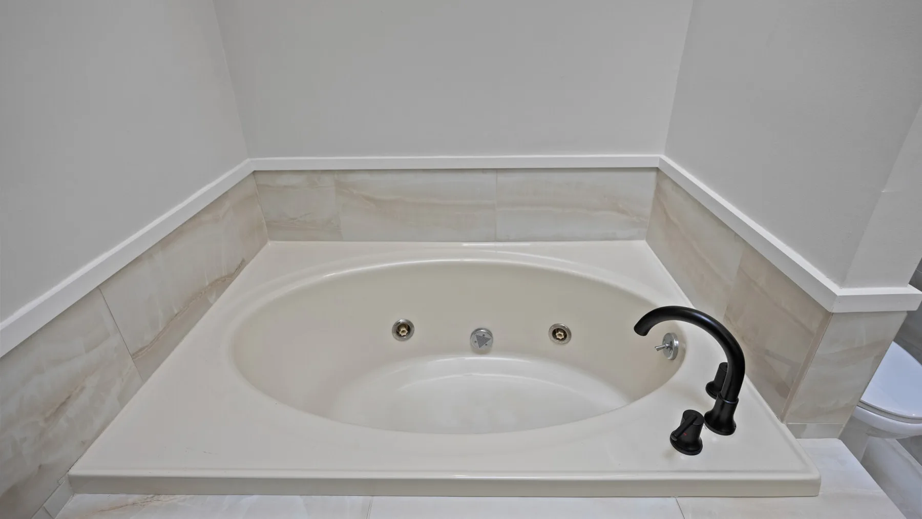 Una bañera empotrada con un grifo oscuro está junto a una pared revestida de azulejos.