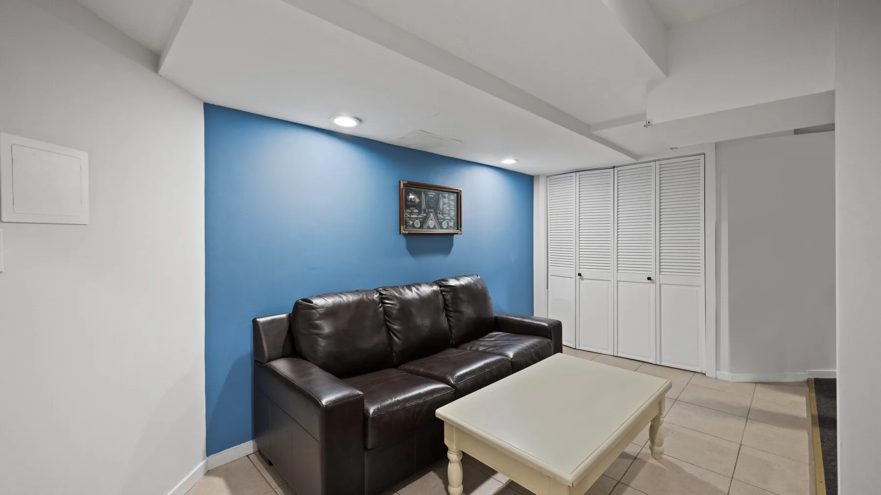 Una sala de estar con asientos oscuros, una mesa de centro blanca y una pared azul.