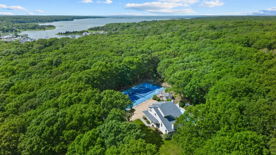 Una vista aérea muestra una casa rodeada de denso bosque verde cerca de un lago.