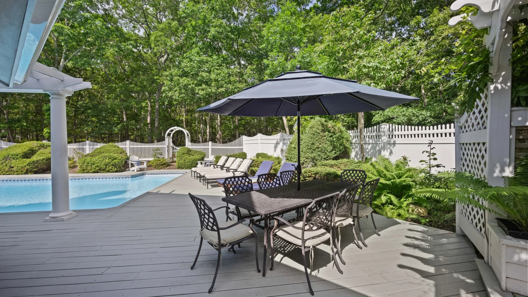 Una terraza exterior con mesa de comedor y sombrilla junto a una piscina.