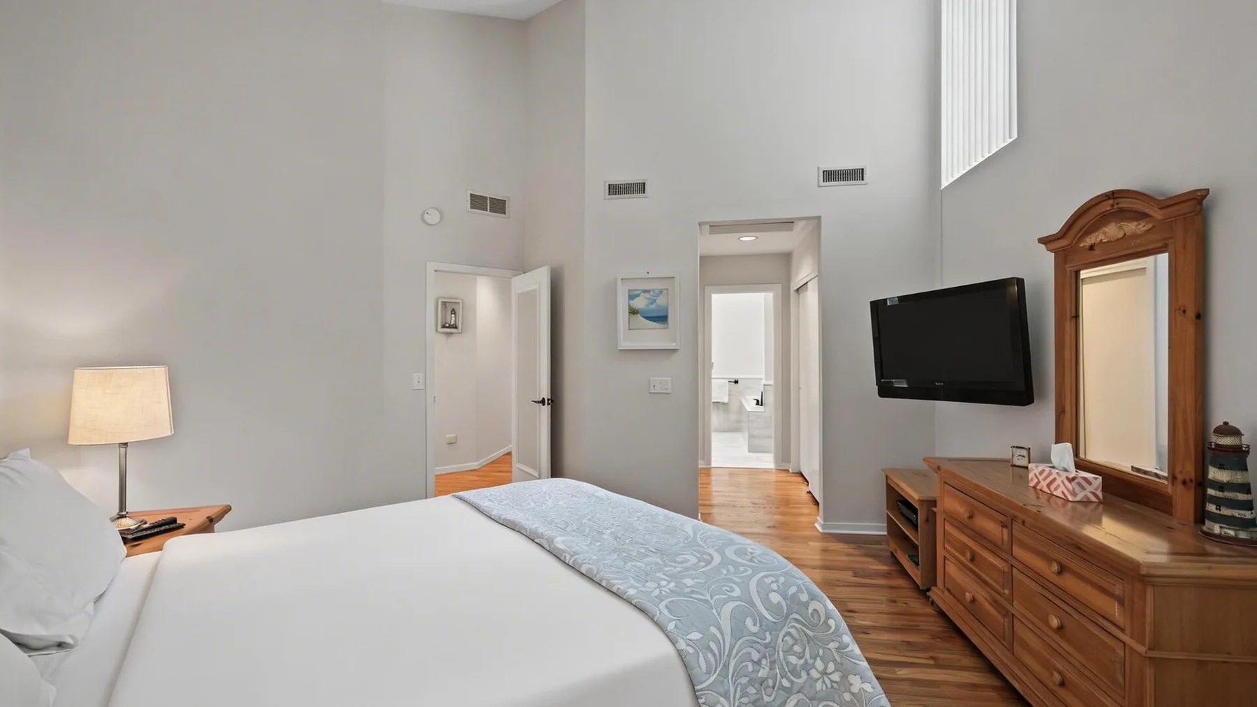 Dormitorio con cama, cómoda de madera y televisor montado en la pared.