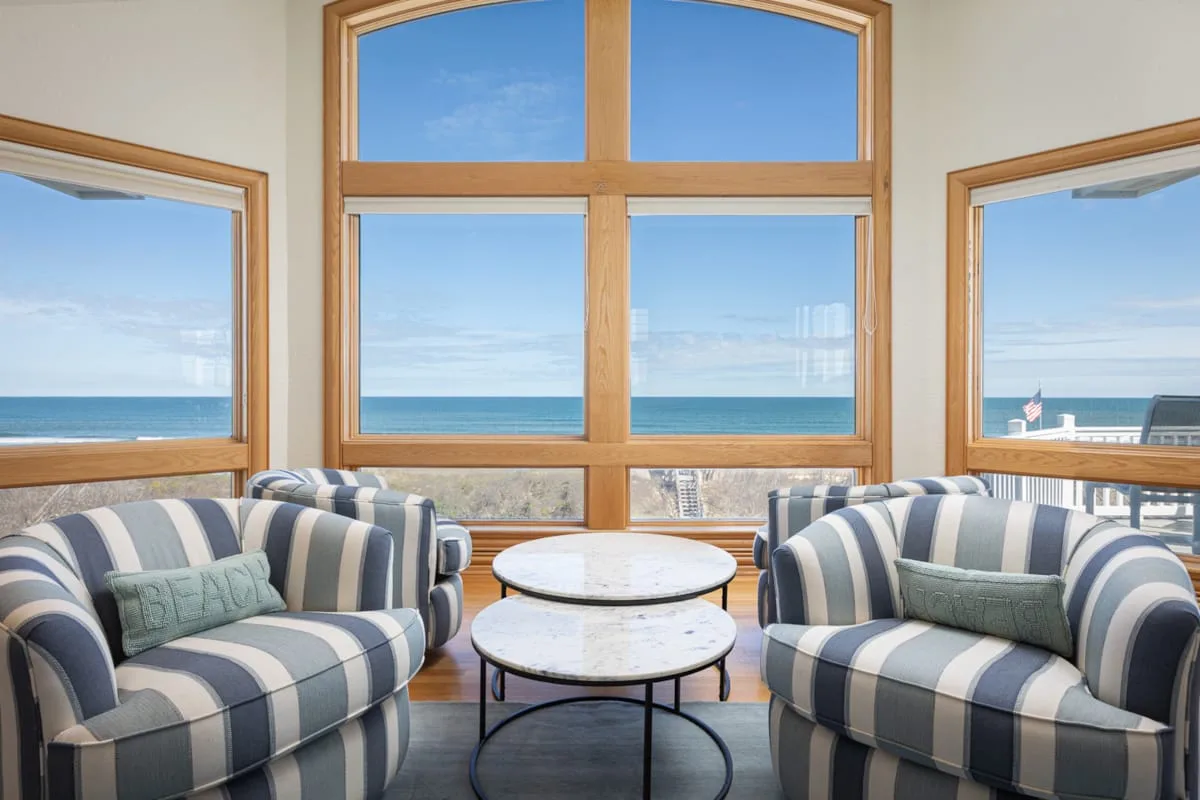 Una sala de estar con asientos a rayas y grandes ventanas con vista al mar.