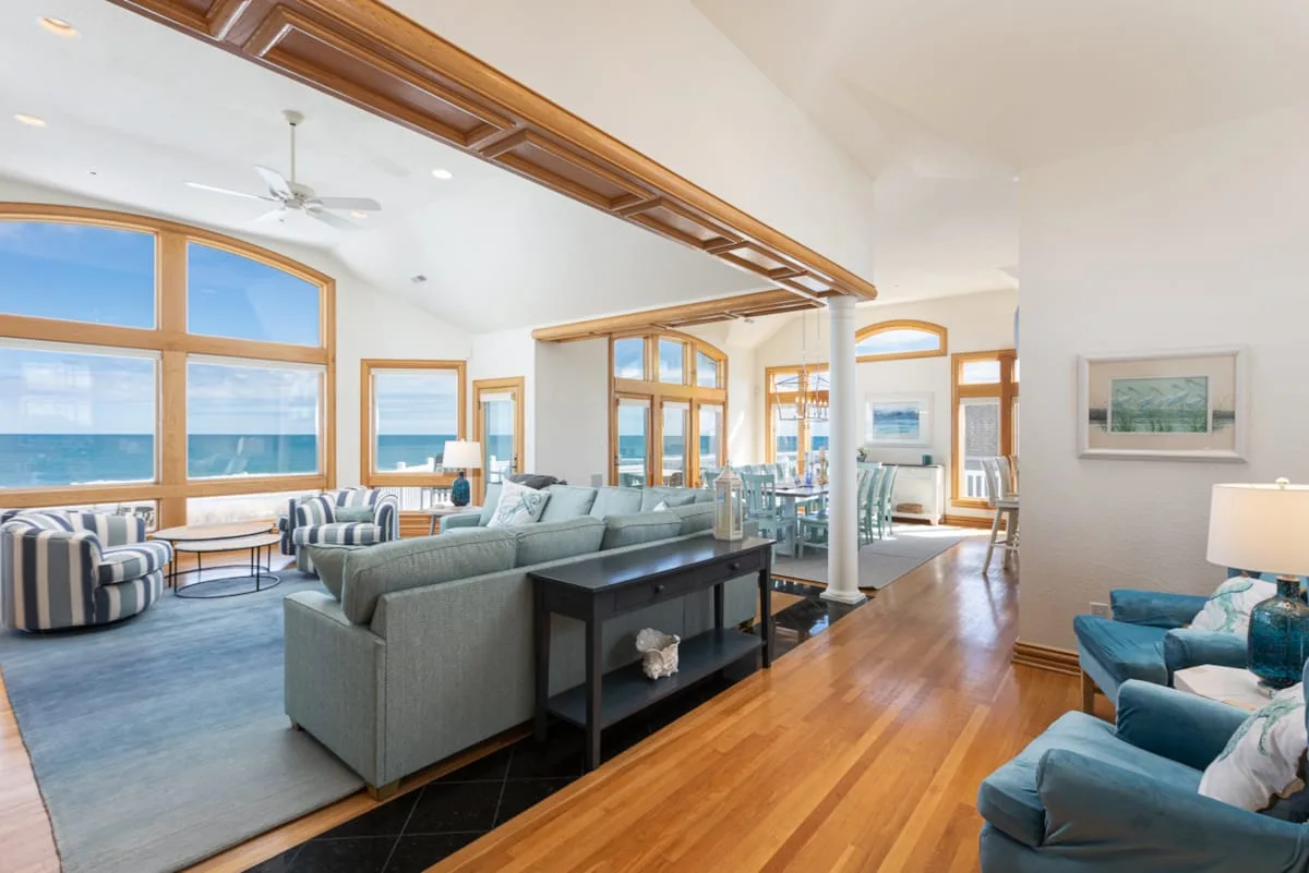 An open living room with seating arranged beside large windows overlooking the ocean.