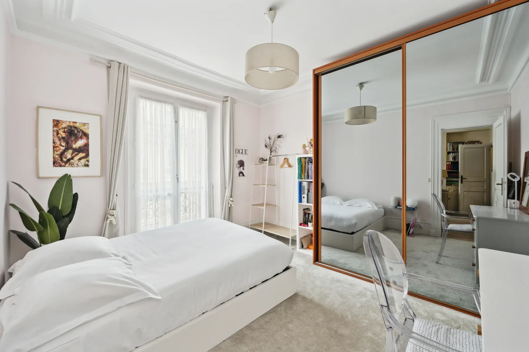 A bright bedroom with a white bed, tall windows, and mirrored wardrobe doors.
