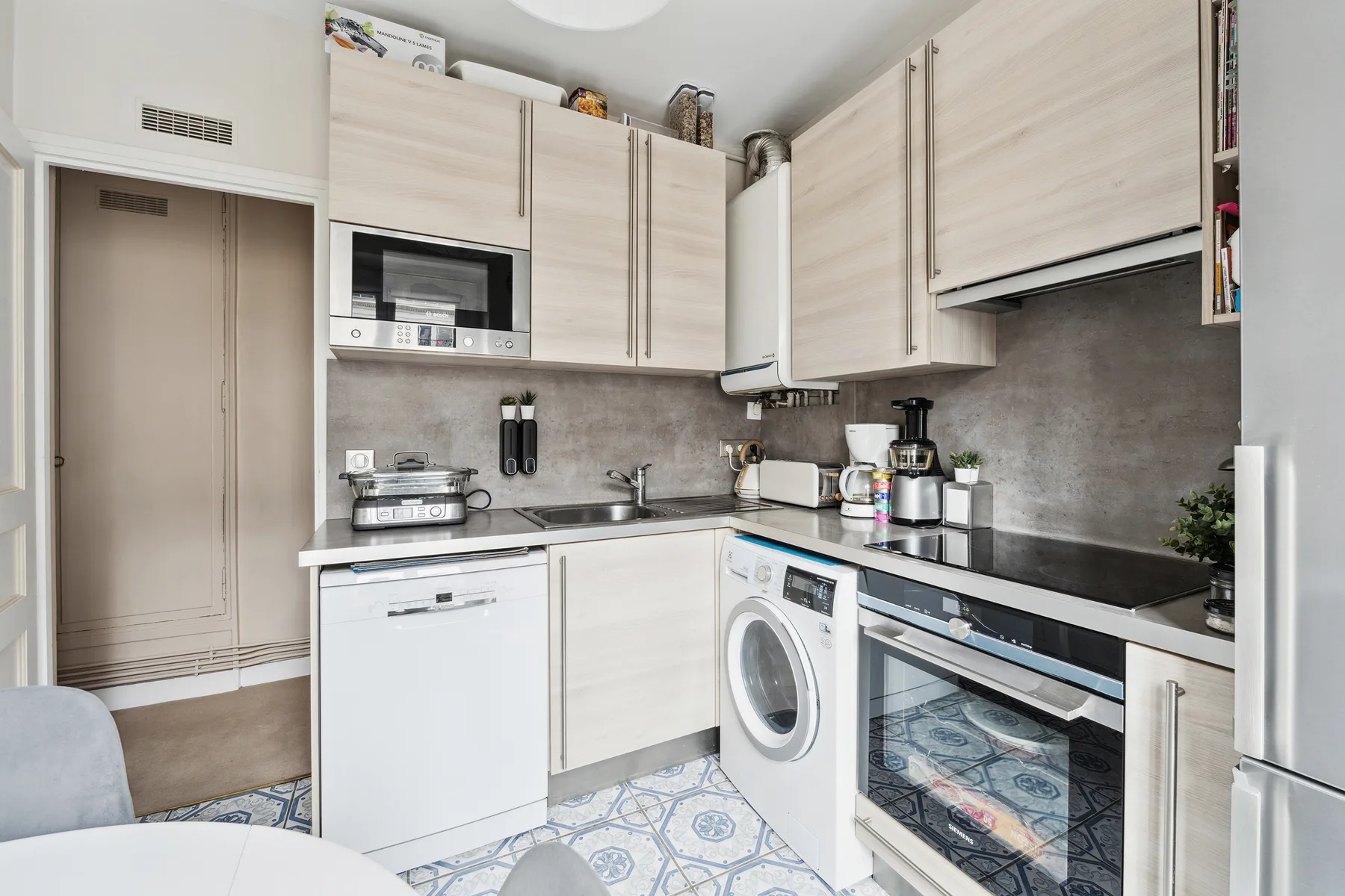 A compact kitchen with pale cabinets, black countertops, and a washing machine.