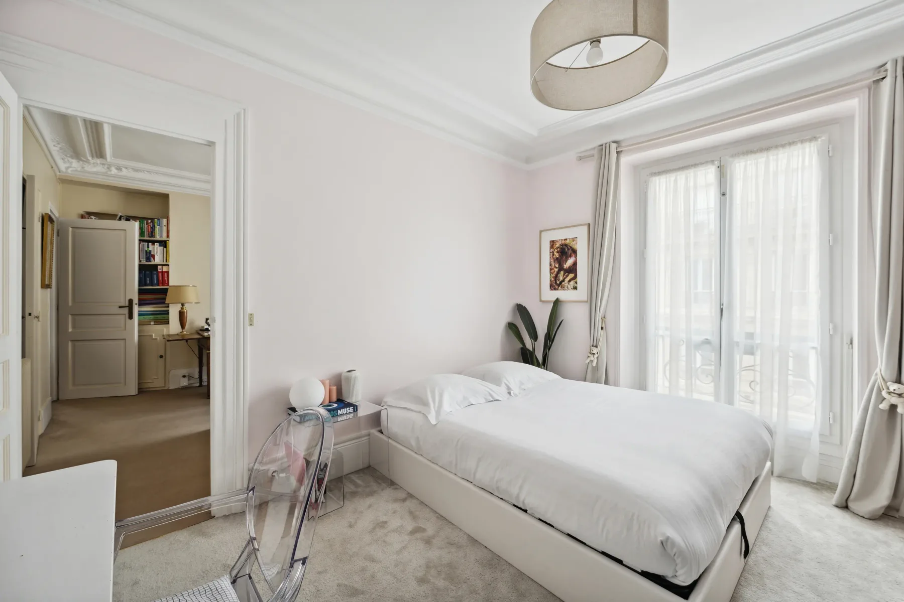 A bright bedroom with a white bed beside tall curtained windows.