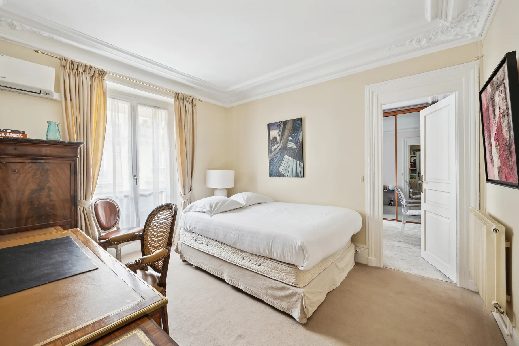 A bright bedroom with a bed, tall windows, and an open doorway.