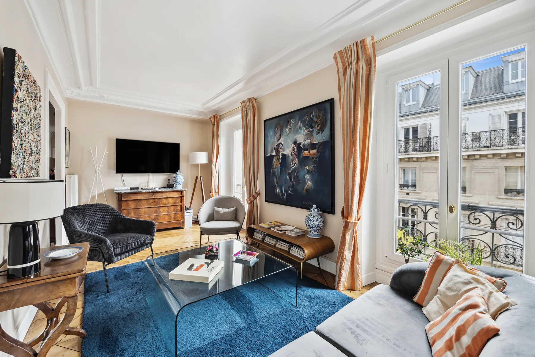 A bright living room with seating, a glass coffee table, and tall windows.