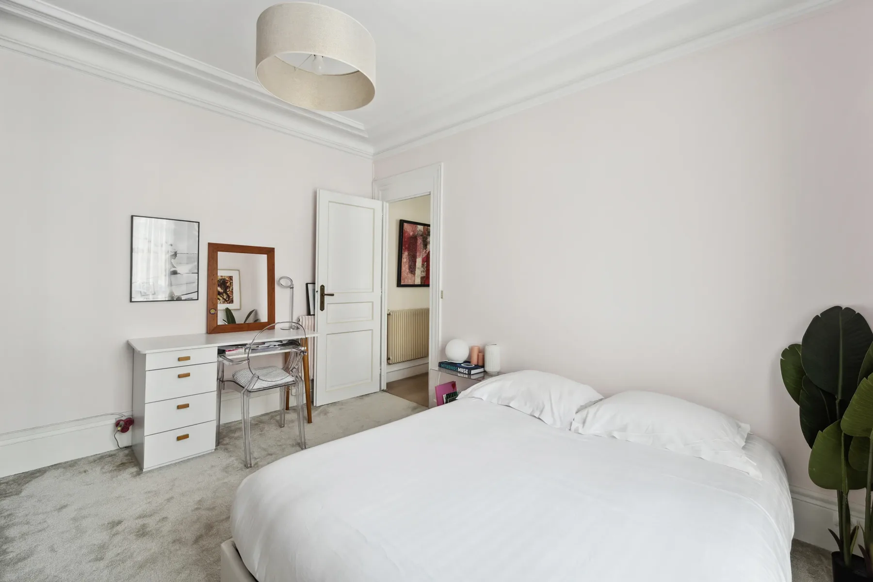 A bright bedroom with a white bed, a desk, and a potted plant.