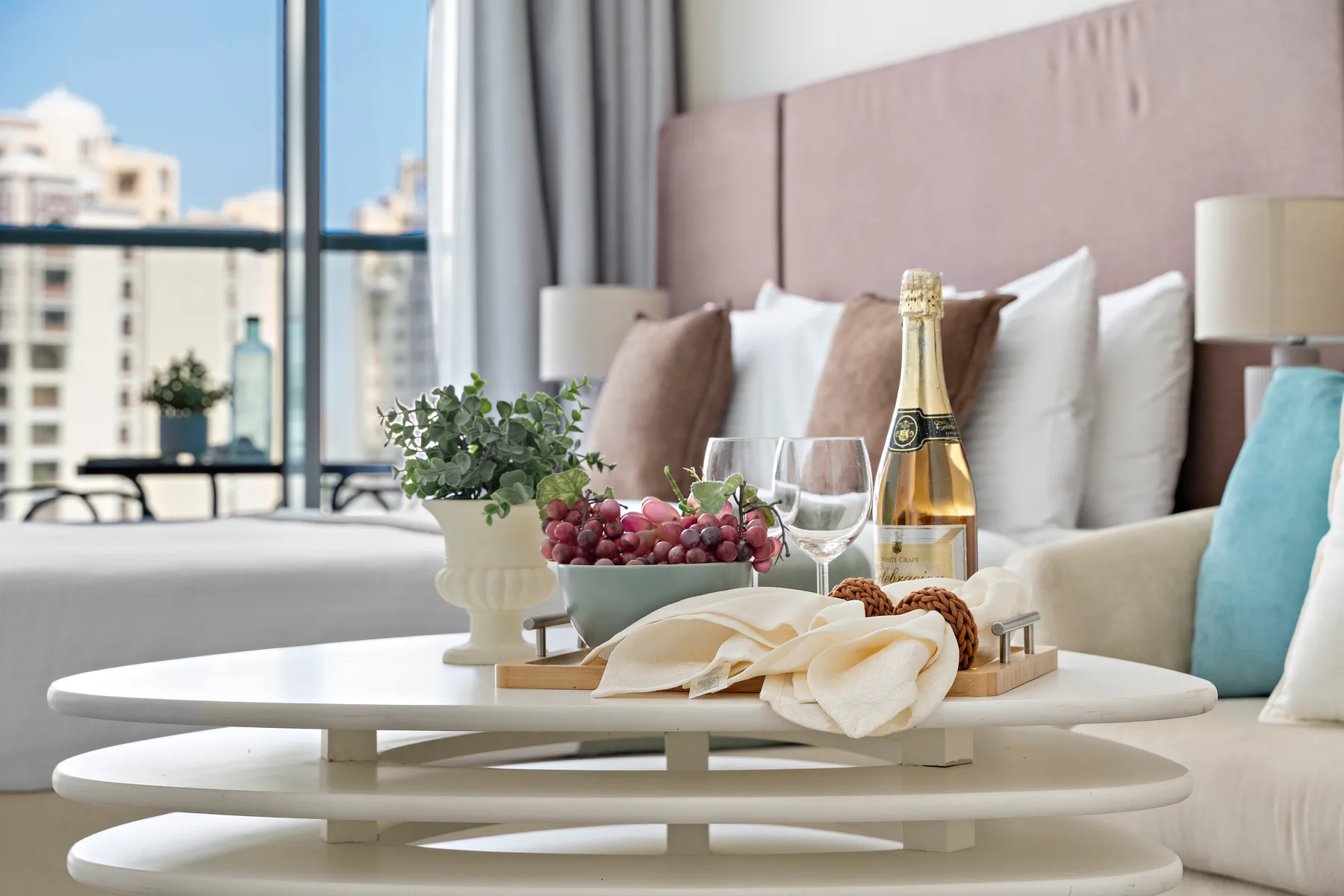 Una zona de estar en un dormitorio, con una mesa preparada con fruta, copas y una botella.