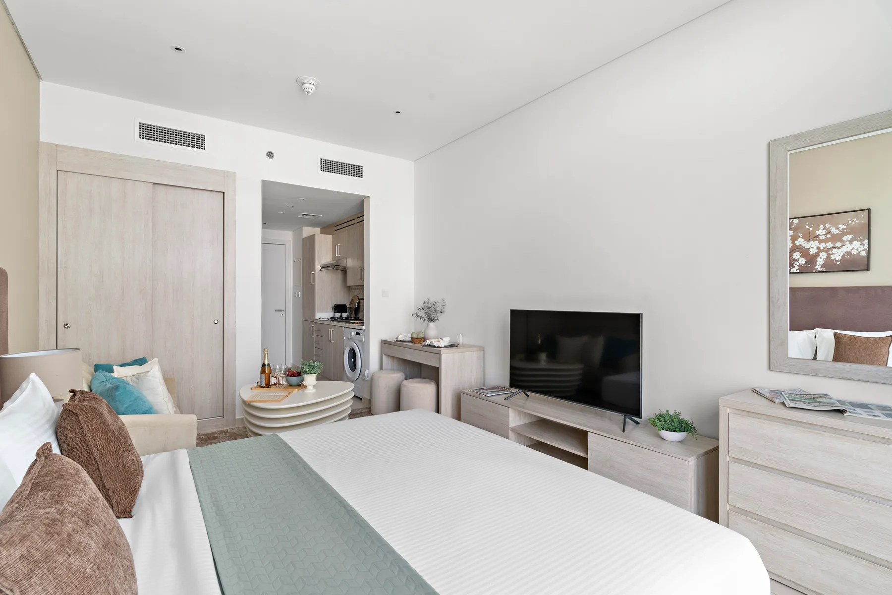 Un dormitorio luminoso con una cama, un televisor y una puerta abierta hacia la zona del baño.