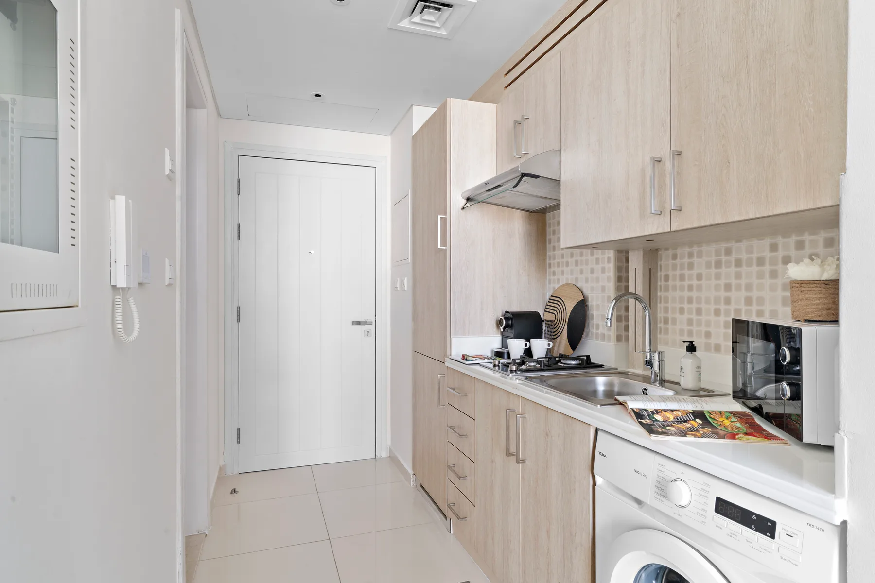 Una cocina compacta con gabinetes de madera clara, un fregadero y una lavadora.