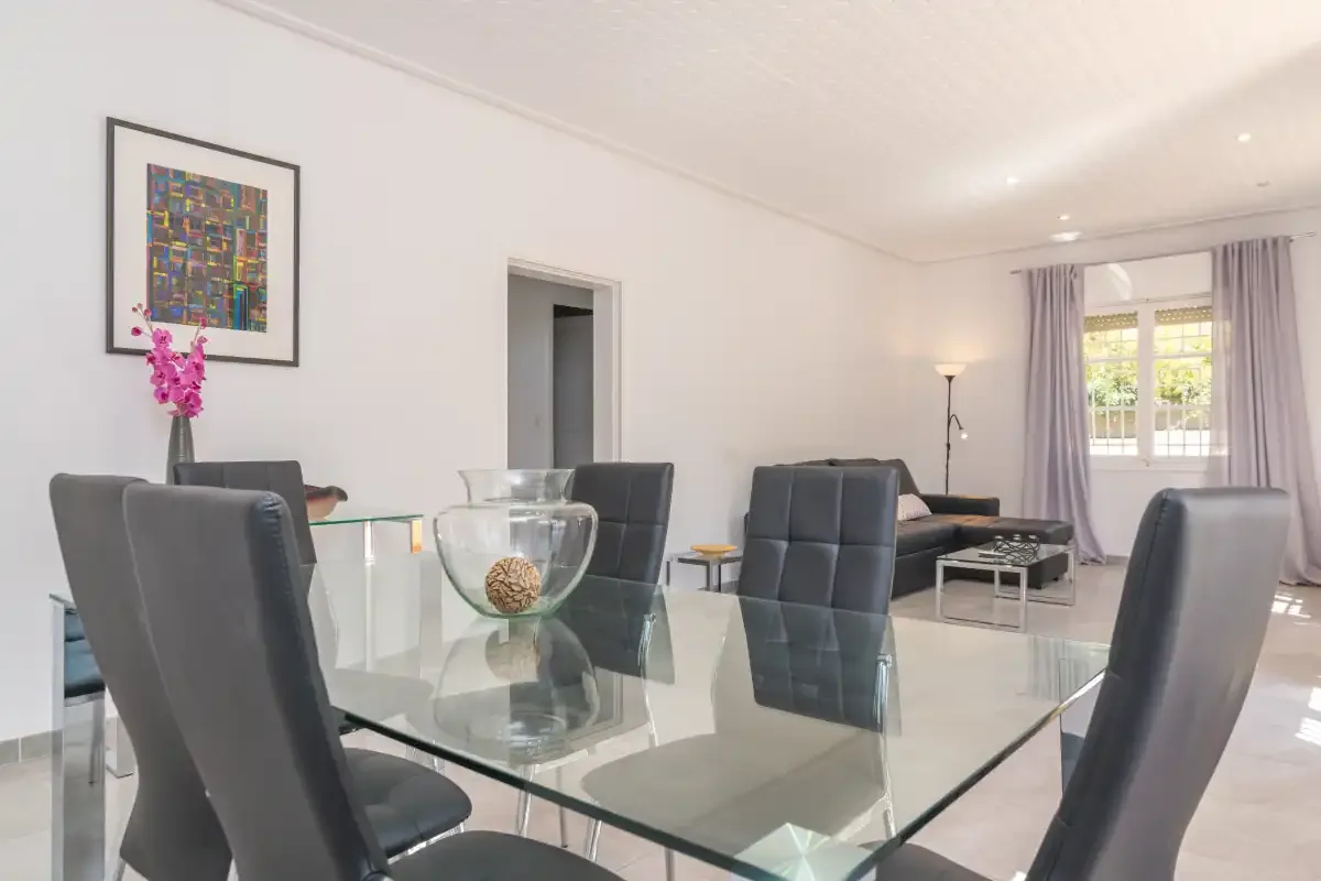 A dining area with a glass table and seating beside a living area.