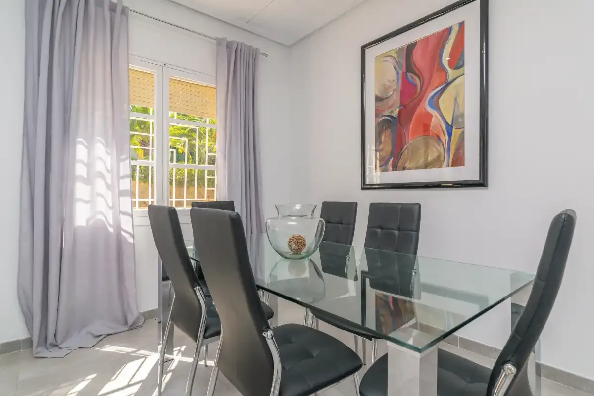 A dining area with a glass table, dark seating, and colorful wall art.
