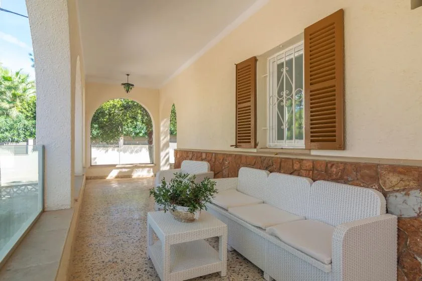 A covered patio with white seating, a small table, and open arched views.