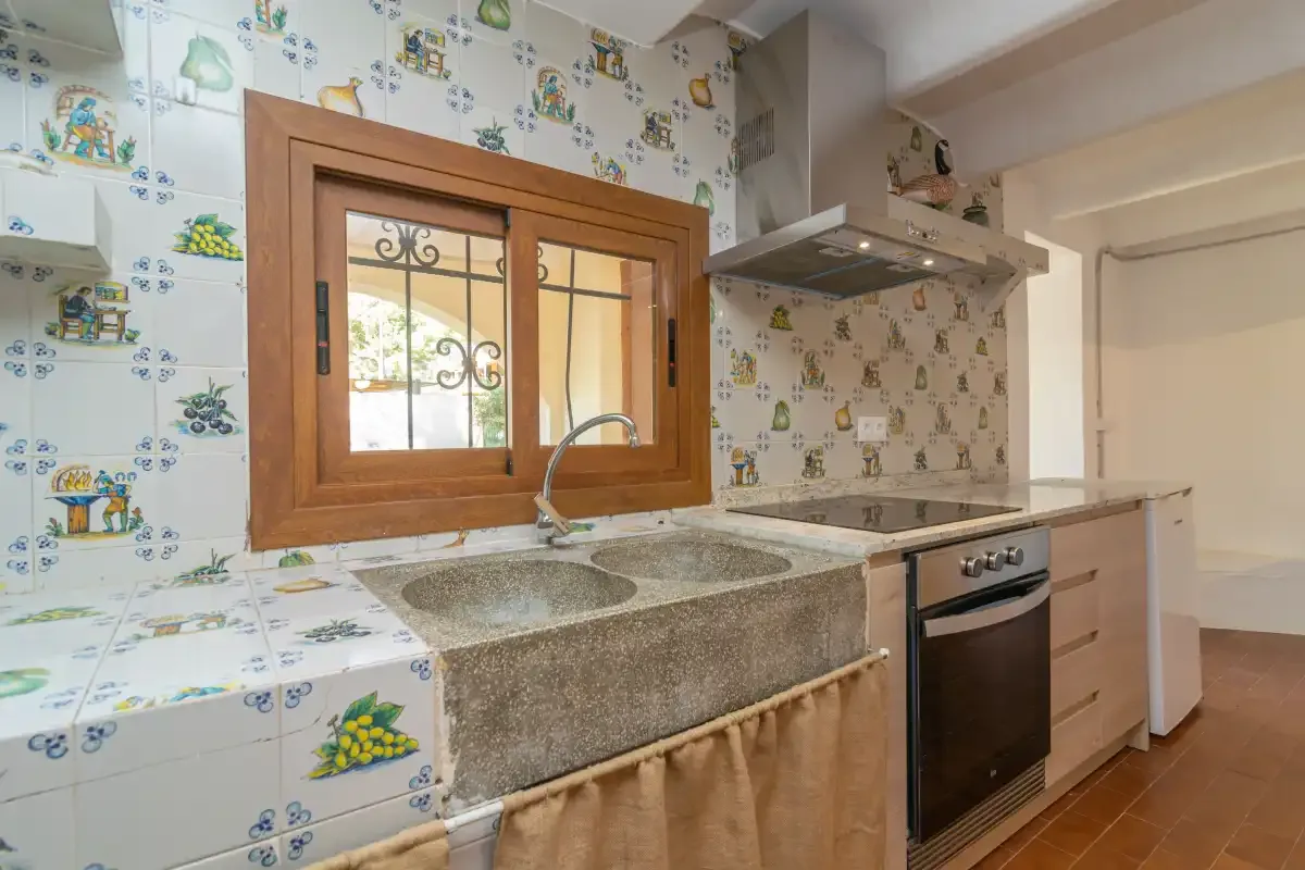 A tiled kitchen with a sink beneath a wooden-framed window.