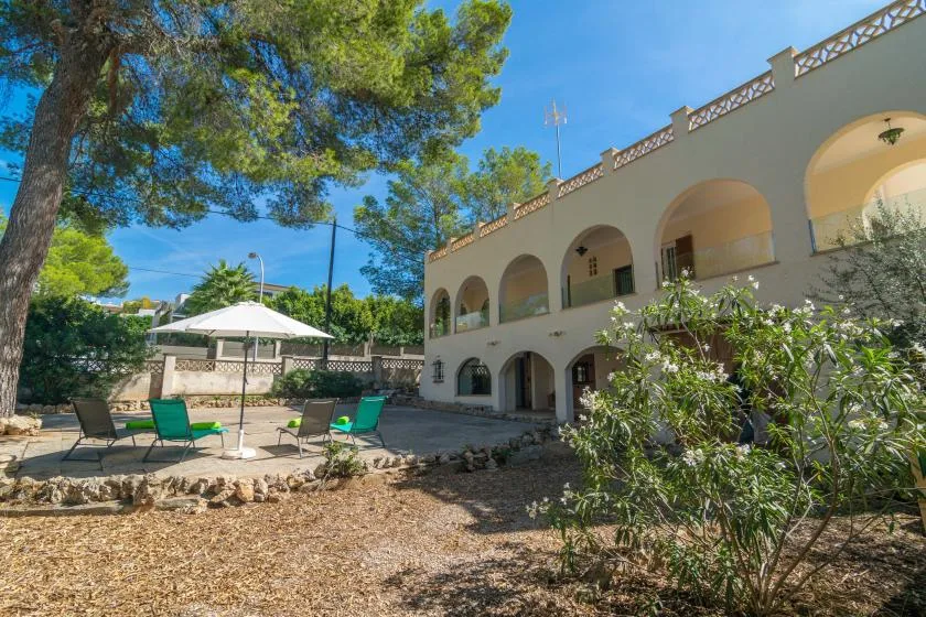 A sunny courtyard with outdoor seating beside a two-story building with arched openings.
